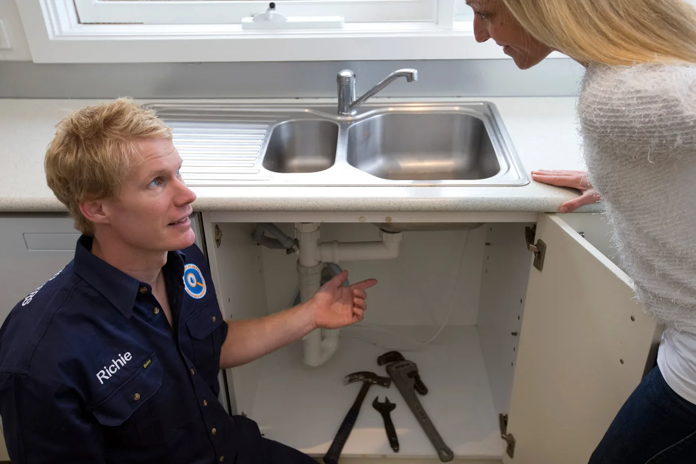 A Fix-It Right plumber showing a homeowner the pipes under the kitchen sink