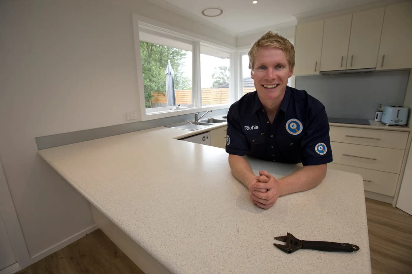 Richie leaning on a kitchen benchtop, adjustable wrench beside him