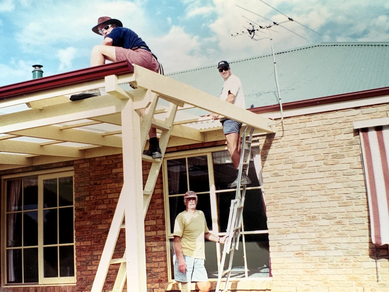 Richie installing roof sheets on the rear verandah of the Langwarrin house, with his dad Paul on the ladder and his grandad Donald watching from below.