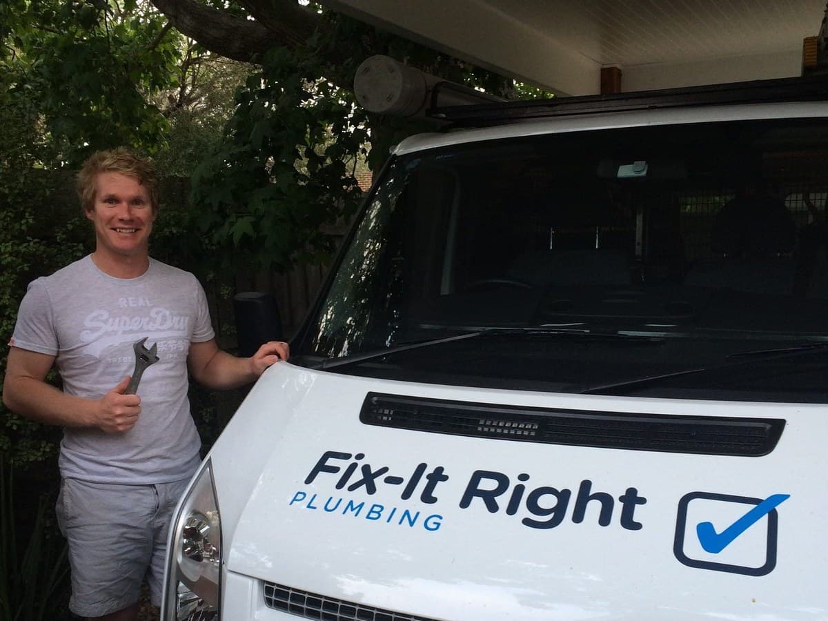 Richie Foster holding an adjustable wrench beside a Fix-It Right Plumbing van