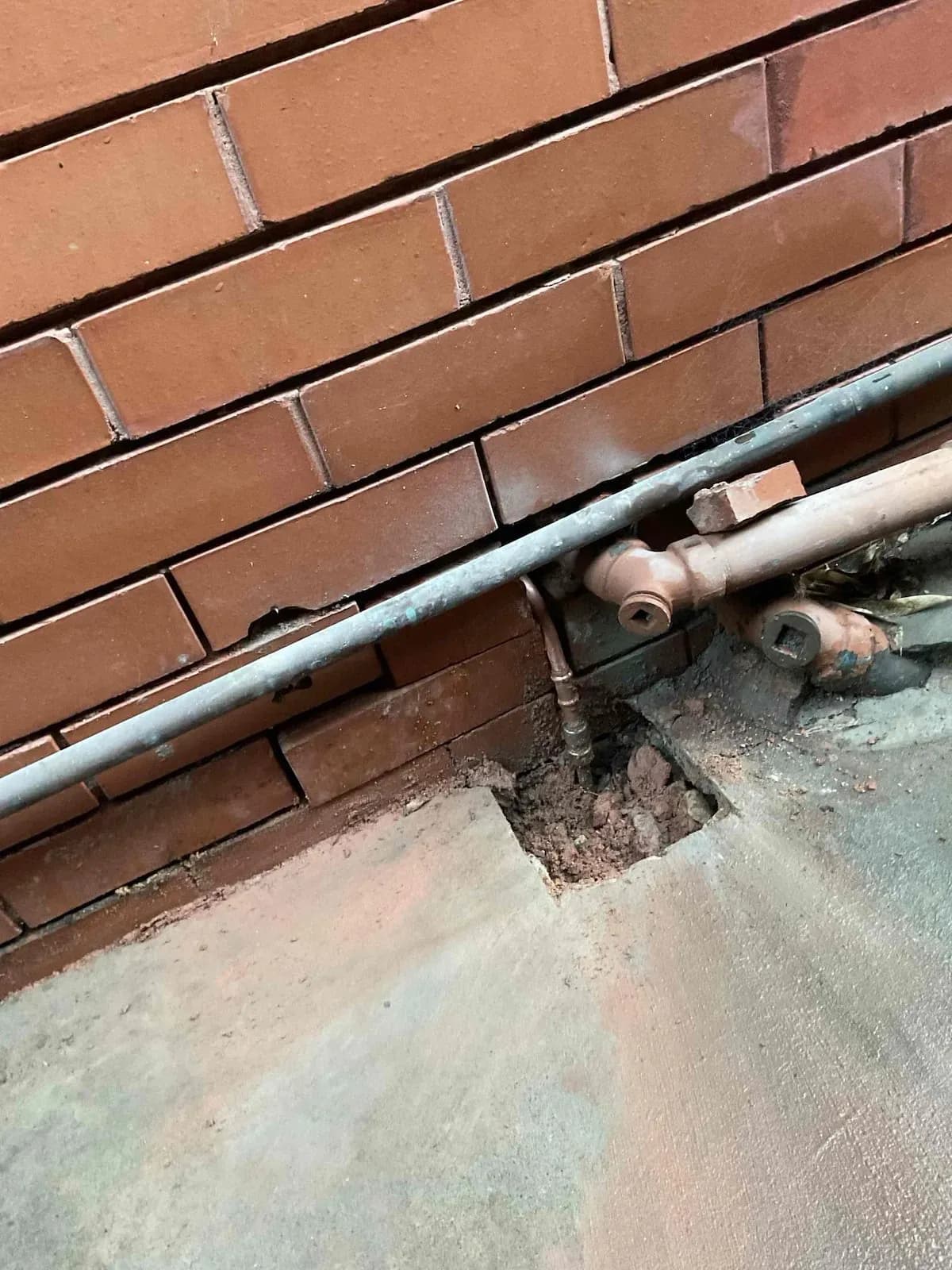 Copper water pipe running along a brick wall with the ground opened up