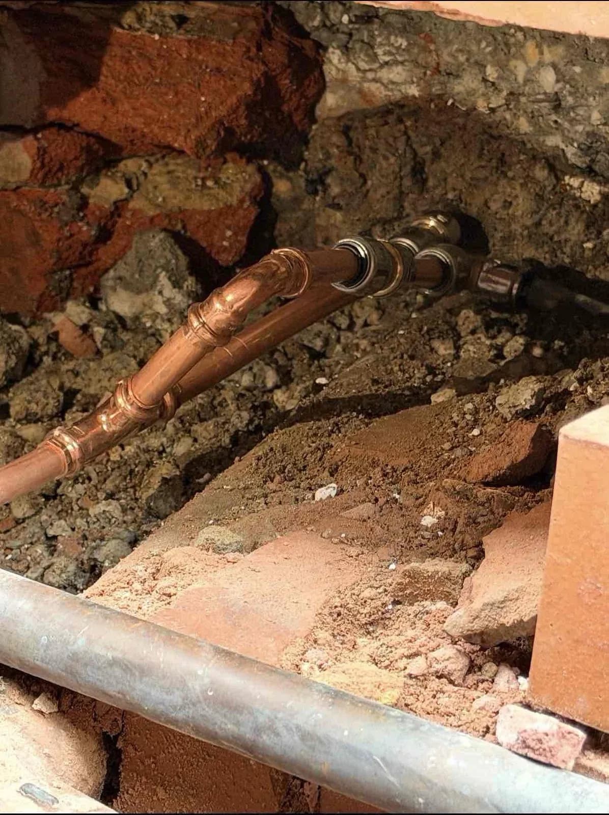 New copper pipe sections fitted below ground beside the wall