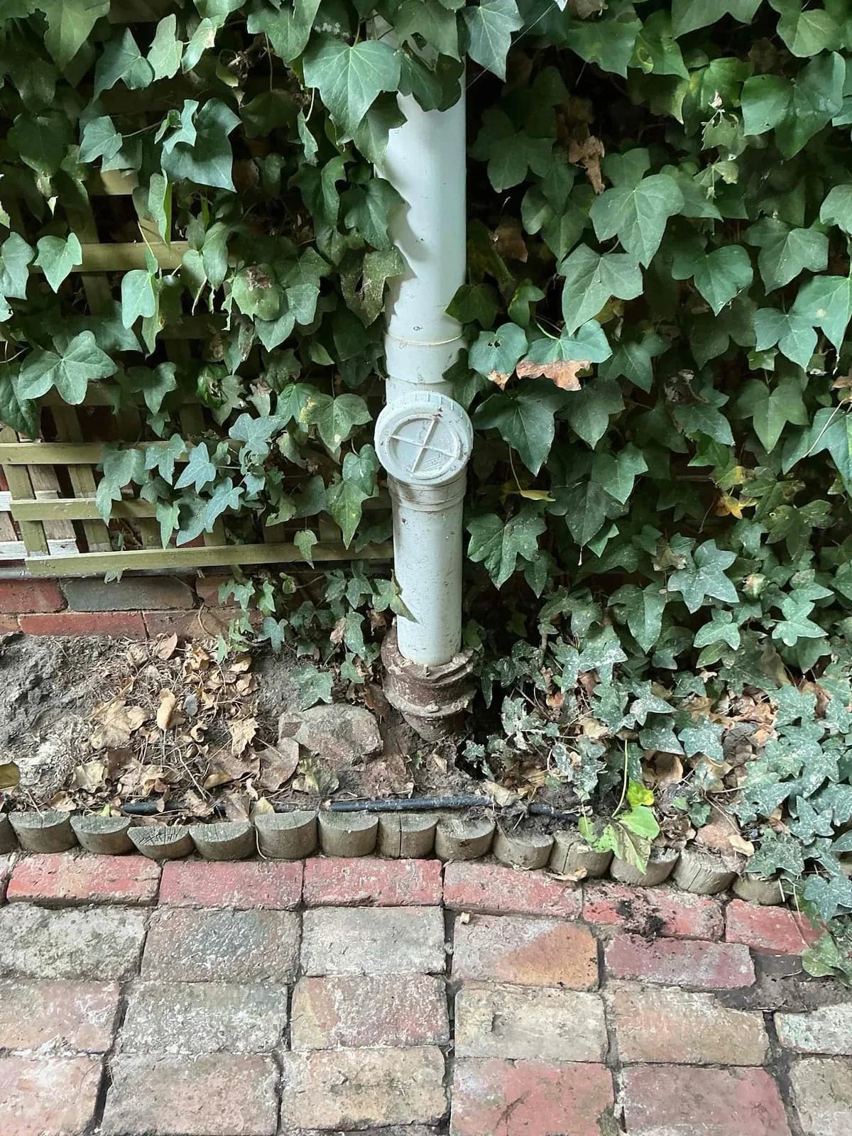 Old drain riser and inspection opening beside a brick wall