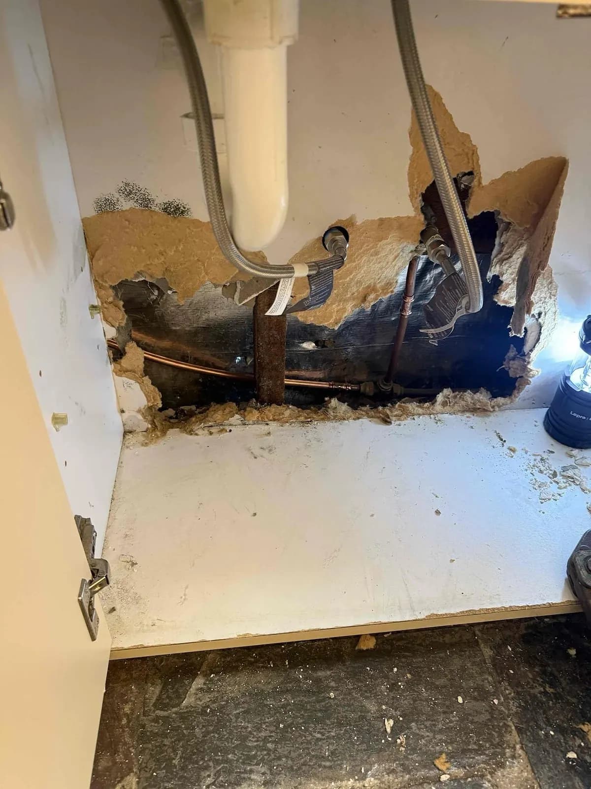 Leaking copper pipe exposed in the wall behind the cabinet