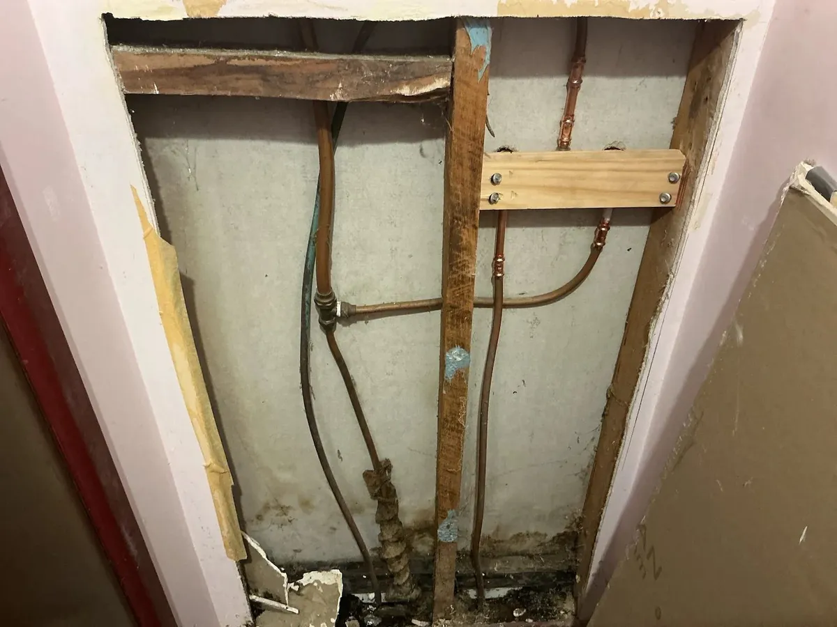 Old shower breach and pipes exposed behind the wall
