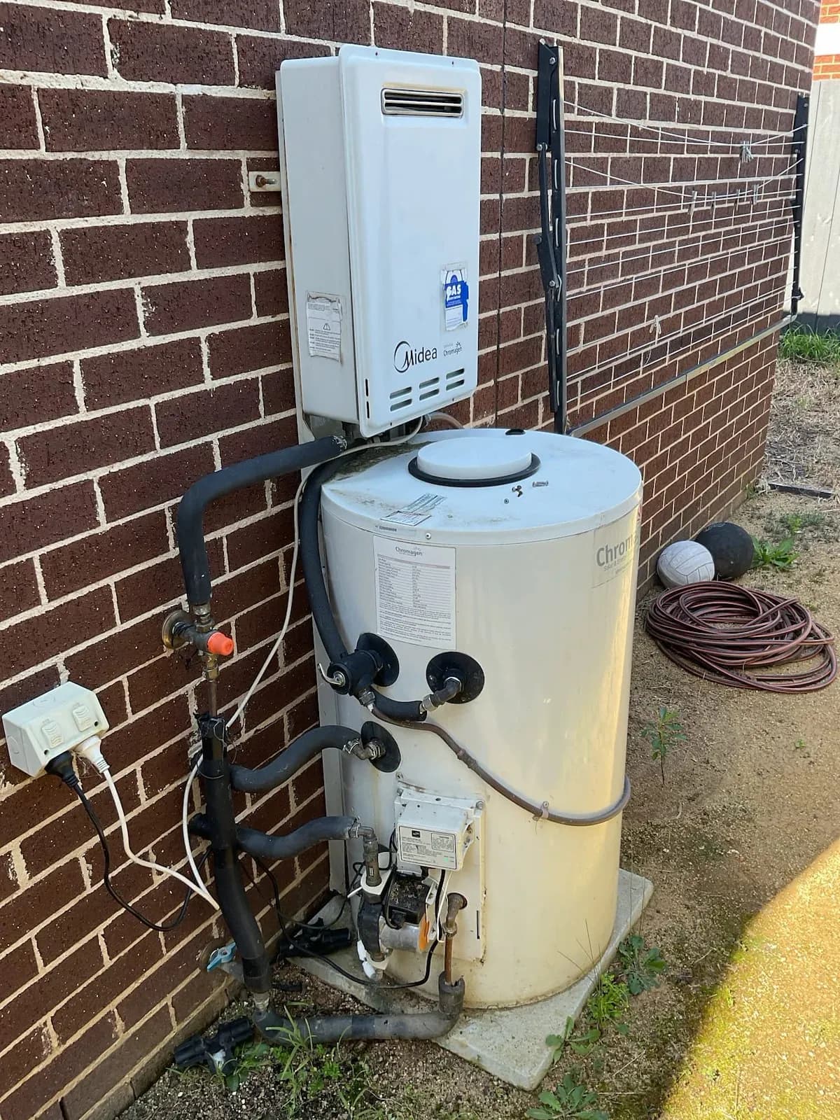 Old solar storage hot water system with a gas booster on a brick wall
