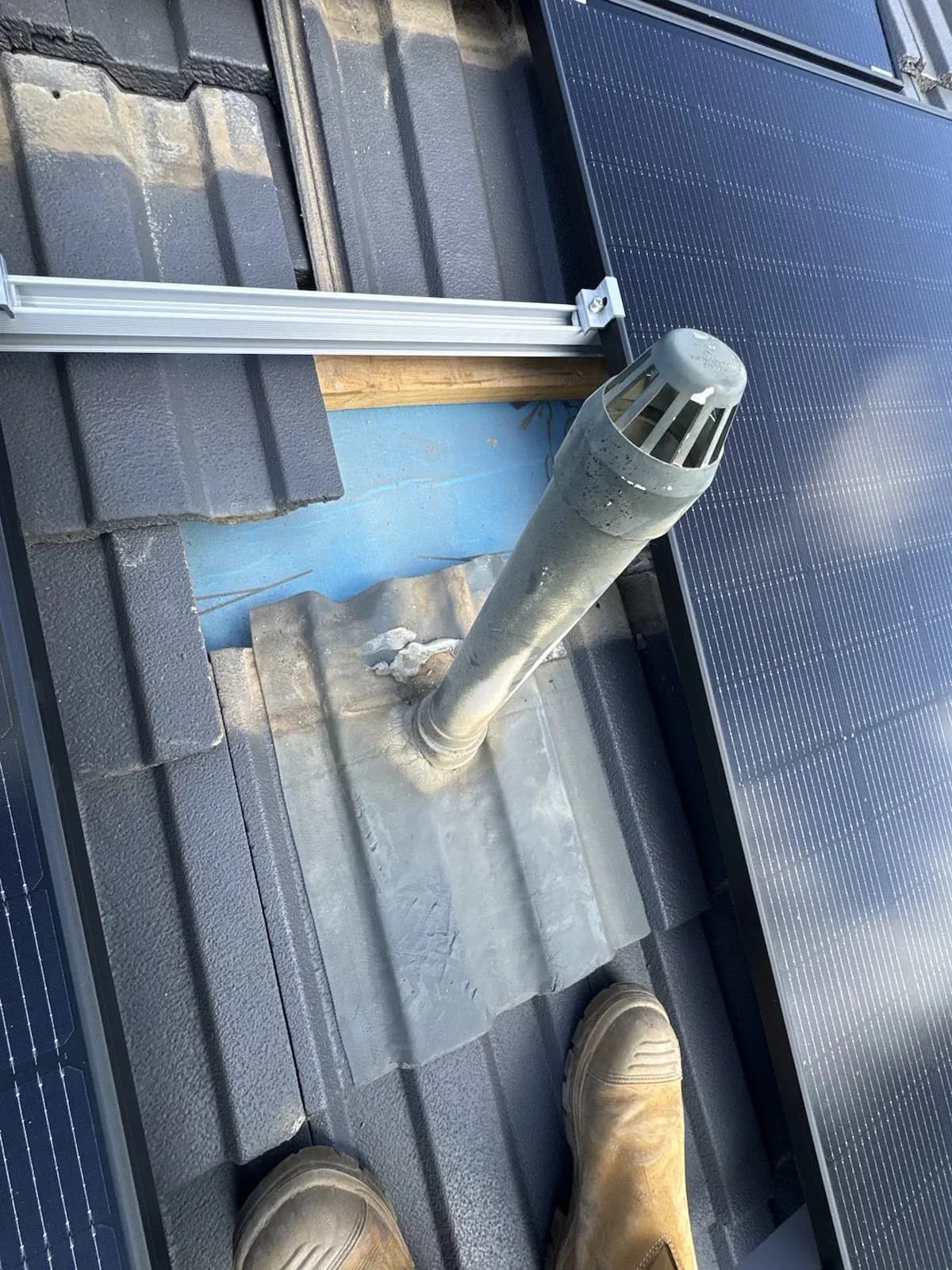 Old roof flashing around a vent pipe among solar panels