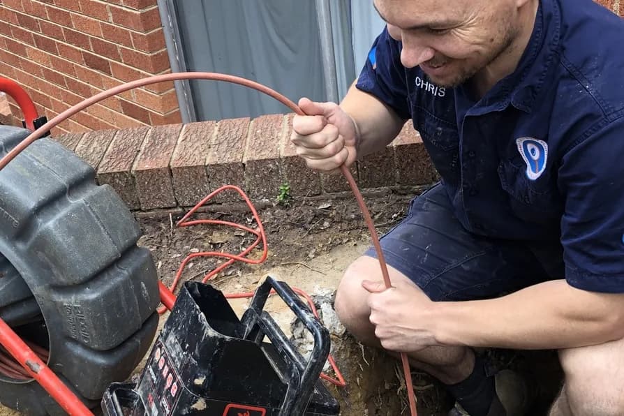 A Fix-It Right plumber feeding a drain camera into an open sewer inspection pit to find the cause of a blockage