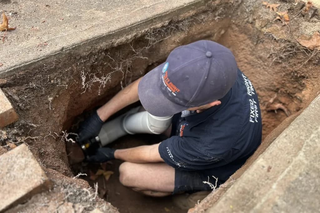 A Fix-It Right plumber fitting a new section of pipe in an inspection pit