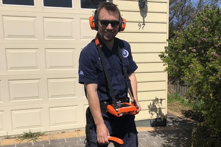 A Fix-It Right plumber on a driveway with an acoustic leak-detection listener, tracing a hidden water leak
