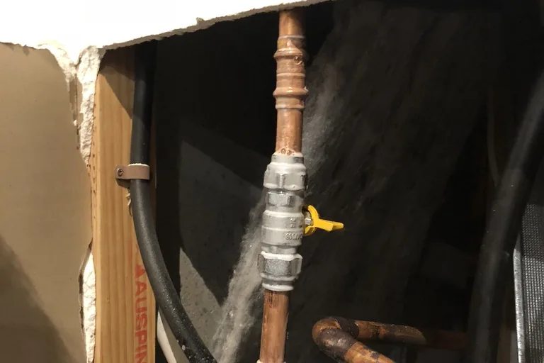 A copper water pipe and valve inside an opened-up wall cavity, where a hidden leak runs out of sight