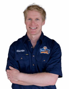 Plumber wearing a navy blue Fix-It Right Plumbing uniform, with the Fix-It Right Plumbing logo, with the name Richie embroidered on it, standing with arms crossed.
