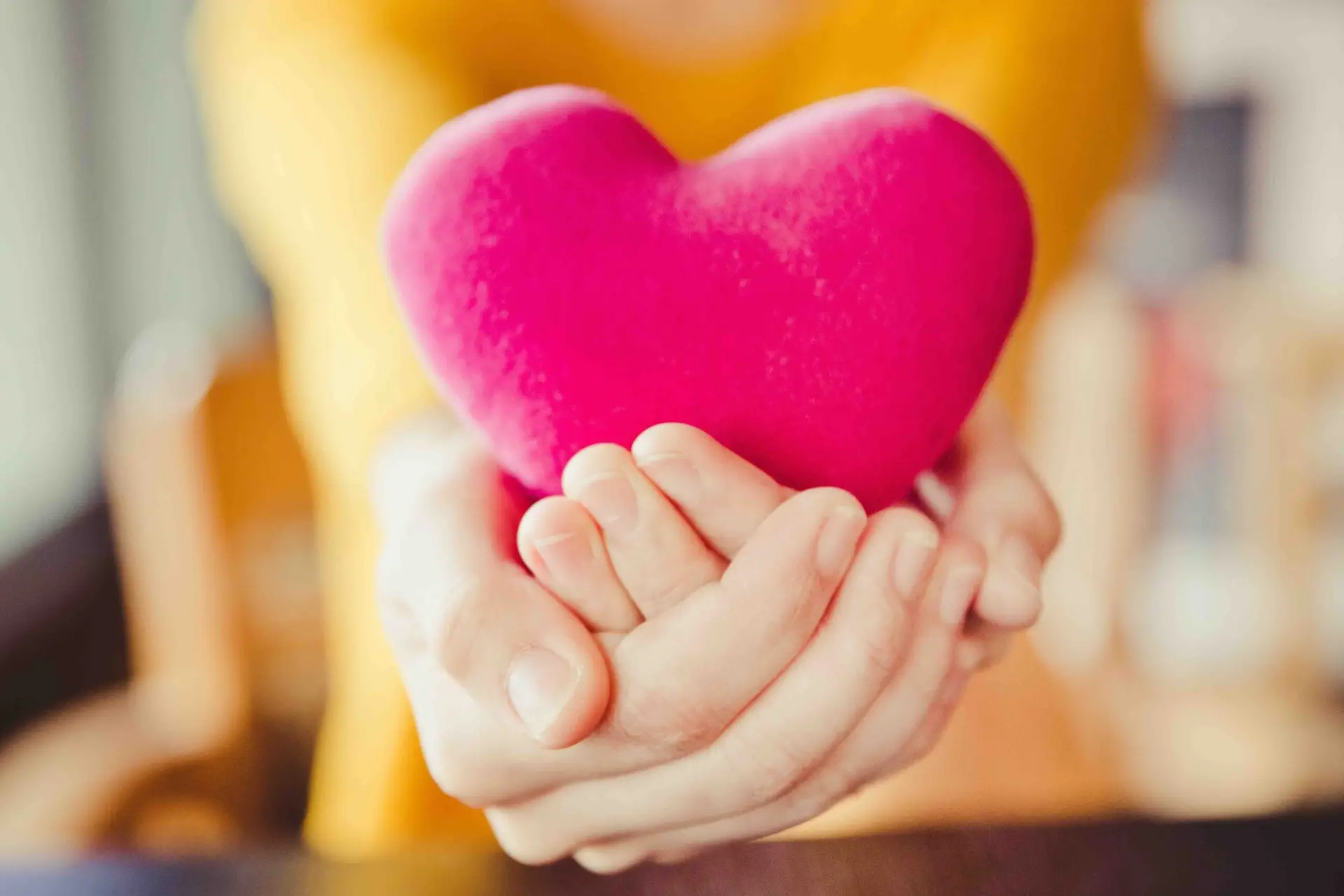 Hands holding a soft, pink, heart-shaped object, with a blurred yellow background—perfectly capturing the care and warmth at George and Mums Plumbing.
