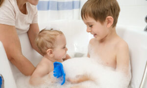 baby boy and older brother washing and playing in hot water bath with foam.